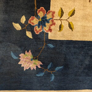 Textured pile rug showing a navy field with stylized multicolored flowers and a wide tan border.