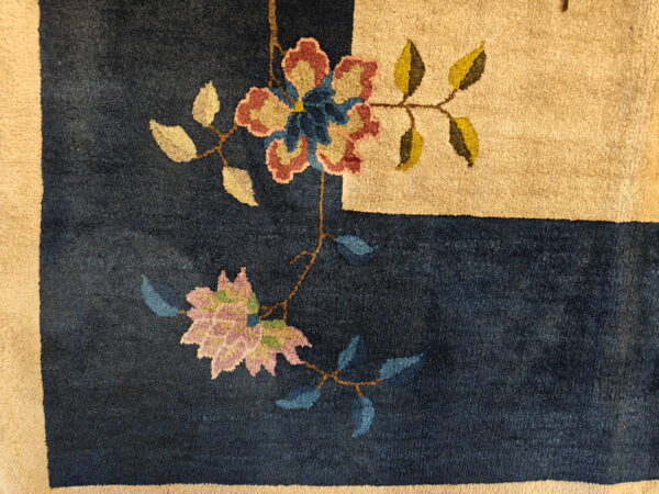 Textured pile rug showing a navy field with stylized multicolored flowers and a wide tan border.