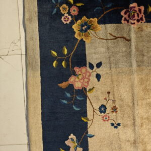 Navy bordered rug with a beige field and colorful floral design lies on cracked light tile flooring.