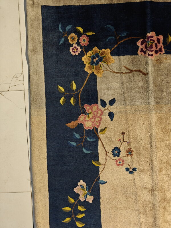 Navy bordered rug with a beige field and colorful floral design lies on cracked light tile flooring.