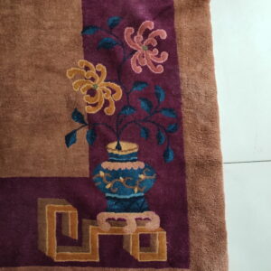 High pile rug in rust and maroon featuring a floral vase and geometric stand motif on white tiled flooring.