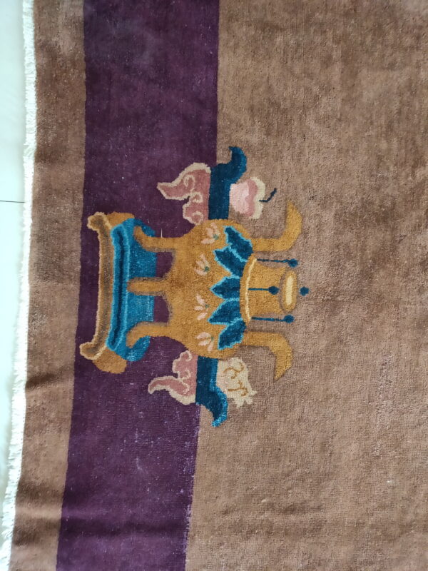 Brown rug with a purple stripe features a gold, teal, and pink stylized figure on white tile flooring.