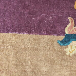 Detail shot of a rug with purple and tan fields bordering stylized patterns in yellow, blue, and pink.