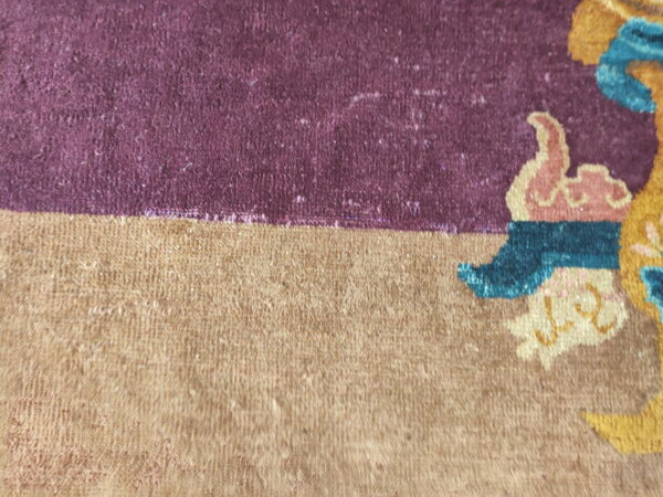 Detail shot of a rug with purple and tan fields bordering stylized patterns in yellow, blue, and pink.