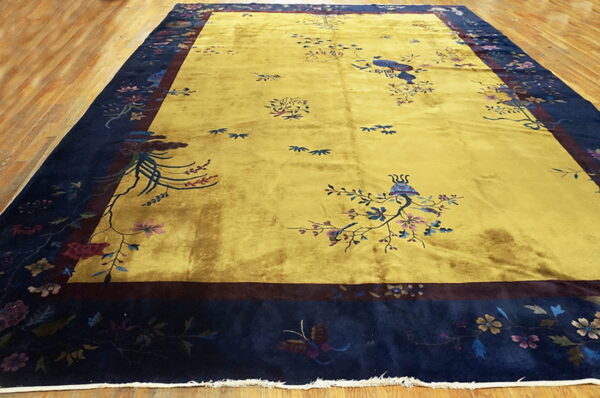 Bright yellow rug with scattered bird and flower patterns and a deep navy border on wood flooring.