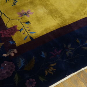 Yellow field rug with a navy floral border, separated by a burgundy stripe, resting on wood.