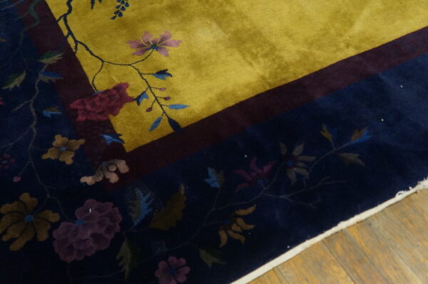 Yellow field rug with a navy floral border, separated by a burgundy stripe, resting on wood.