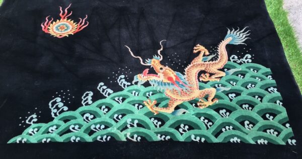 High-pile black rug depicting a colorful dragon over green waves, partially visible on outdoor grass.