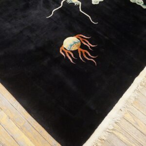 High-pile black rug with colorful patterns and cream fringe rests on light-colored wood floorboards.