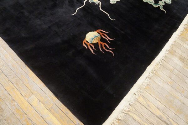 High-pile black rug with colorful patterns and cream fringe rests on light-colored wood floorboards.