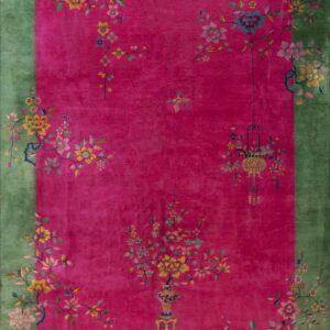 Pink rug with a green border featuring intricate multicolored floral vines, vases, and a hanging lantern.