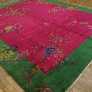 Bright magenta rug featuring scattered floral designs and a wide emerald green border on worn wood floors.