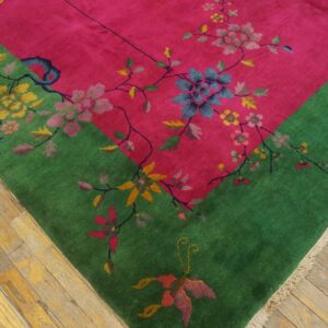Bright pink and green rug with floral and vine patterns rests on worn hardwood planks.