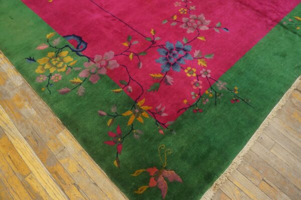 Bright pink and green rug with floral and vine patterns rests on worn hardwood planks.