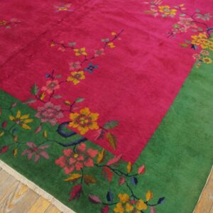 Vibrant pink rug with a green border and multicolored floral pattern, featuring a soft texture on wood plank flooring.