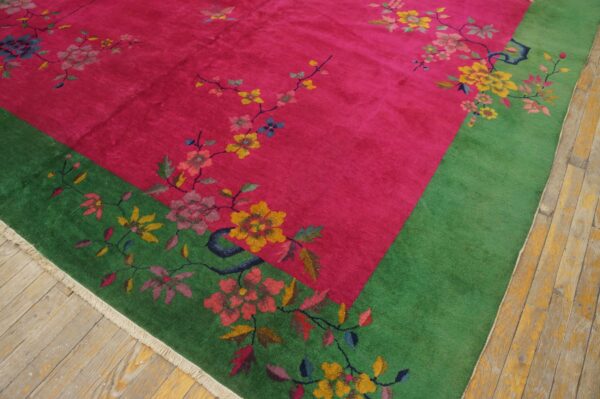 Vibrant pink rug with a green border and multicolored floral pattern, featuring a soft texture on wood plank flooring.
