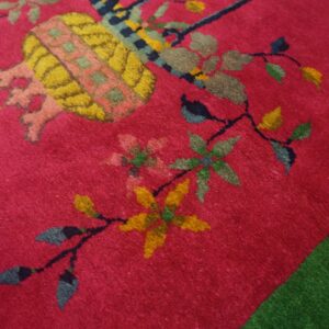 A textured magenta rug with large yellow, pink, and green floral motifs borders a solid green rug.