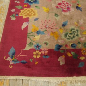 Colorful floral rug with a tan field and red border rests on distressed yellow wooden floorboards.