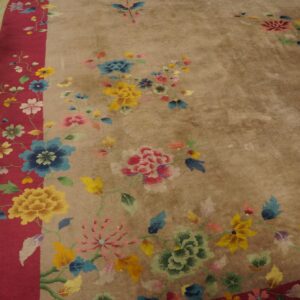 Muted beige rug with bright multicolor florals, a wide red border, resting on yellow wood floors.