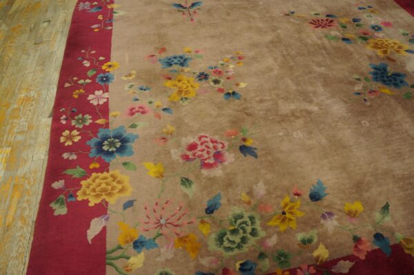 Muted beige rug with bright multicolor florals, a wide red border, resting on yellow wood floors.