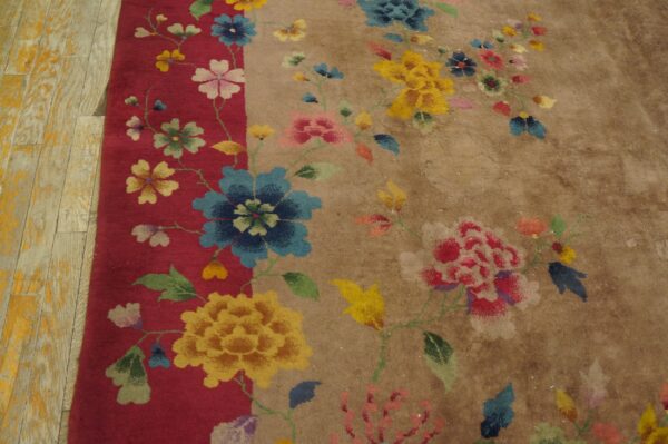 Multicolored floral pattern spans the red border and tan field of a textured rug on worn wood planks.