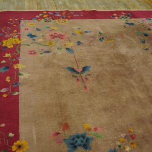 Tan rug with a multicolored floral and butterfly pattern and a wide magenta border on plank wood flooring.