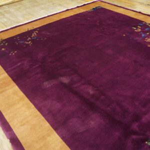 Deep purple high-pile rug with a wide tan border and multicolored floral patterns rests on light wood planks.