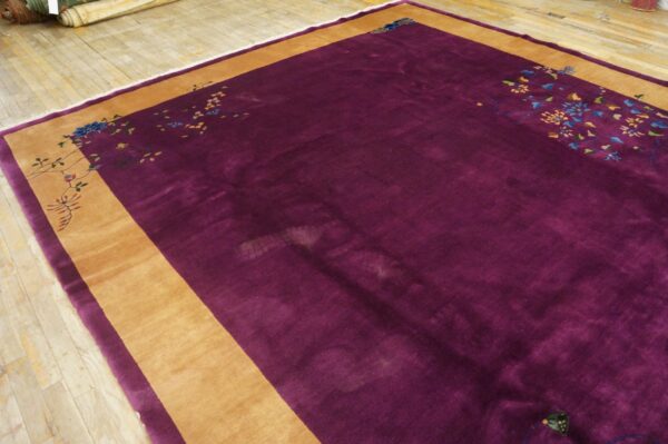 Deep purple high-pile rug with a wide tan border and multicolored floral patterns rests on light wood planks.