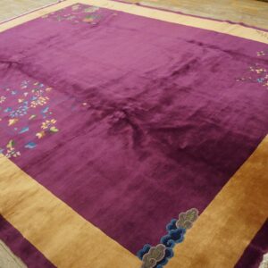 Plush, deep purple rug with a wide gold border and intricate floral corner designs on wood floor.