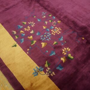 Deep magenta rug with a gold diagonal stripe and multicolored floral details on wood flooring.