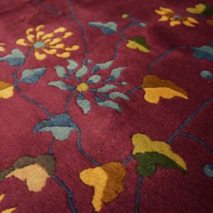 Deep magenta rug with a dense pile and stylized floral patterns in gold, blue, and various greens.