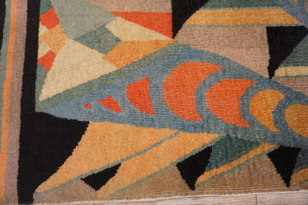 Close-up of a dense rug featuring an abstract geometric design in teal, orange, black, and beige.
