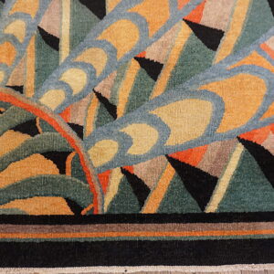 Geometric abstract rug in gold, teal, blue, and black with curved lines and sharp triangles on wood planks.