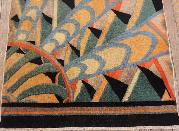 Geometric abstract rug in gold, teal, blue, and black with curved lines and sharp triangles on wood planks.