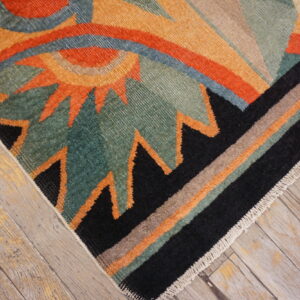 Low-pile rug with geometric orange, teal, and black abstract patterns rests on light wood floors.