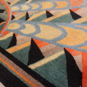 Geometric rug close-up in colors of teal, mustard, black, coral, and blue on wood flooring.