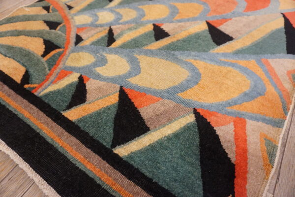 Geometric rug close-up in colors of teal, mustard, black, coral, and blue on wood flooring.