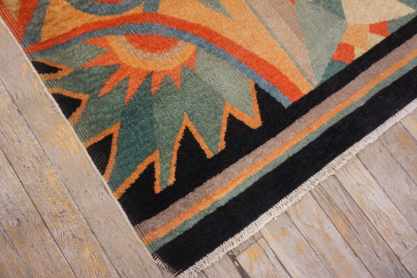 Teal, orange, and black geometric rug with striped border lying on distressed light wood planks.