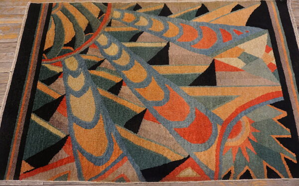 Geometric abstract rug on wood flooring with teal, rust, gold, and black colors and a wide black border.