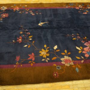 Dark blue rug with a brown border, featuring colorful floral branches, a bird, and set on wood floors.