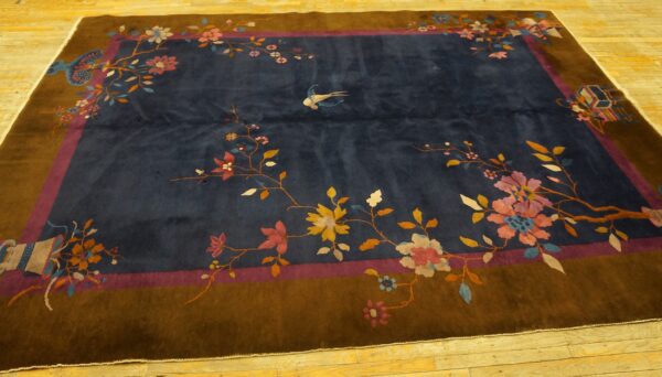 Dark blue rug with a brown border, featuring colorful floral branches, a bird, and set on wood floors.