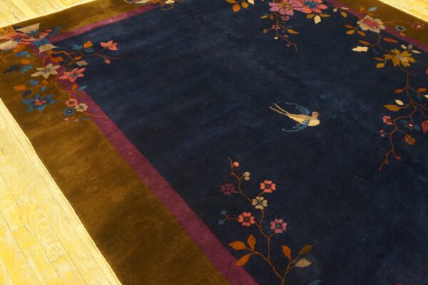 A dark navy blue rug displays multi-colored floral vines and a bird, framed by brown and magenta borders.