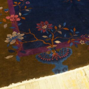 Dark blue and brown high-pile rug with pink floral motifs and fringe rests on light yellow wood flooring.