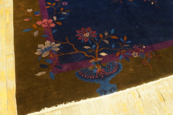 Dark blue and brown high-pile rug with pink floral motifs and fringe rests on light yellow wood flooring.