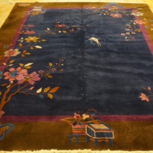 Low-pile blue rug with colorful floral motifs and brown borders rests on distressed yellow hardwood planks.