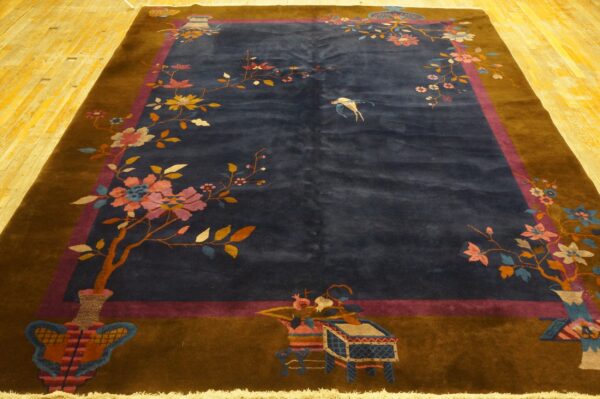 Low-pile blue rug with colorful floral motifs and brown borders rests on distressed yellow hardwood planks.