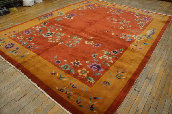 An orange rug featuring multi-colored floral designs and a wide yellow gold border laid on wooden floorboards.
