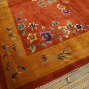 Red-orange floral rug with a gold border featuring bamboo designs rests on worn wooden planks.