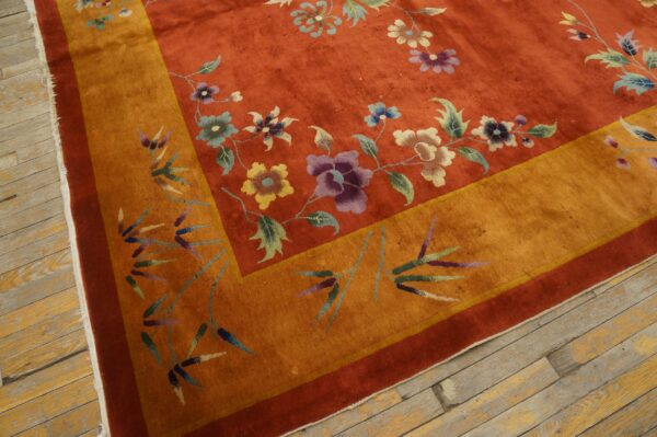 Red-orange floral rug with a gold border featuring bamboo designs rests on worn wooden planks.