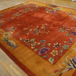 Rust-colored rug with multicolored floral design, a golden-orange border, and white fringe on wood planks.